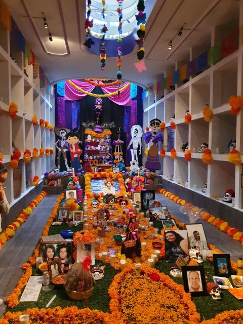 Altar de Día de Muertos dentro del edificio de nichos: fotografías, veladoras y figuras de catrines sobre un tapete de cempasúchil