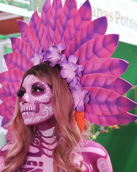 Retrato de una catrina con el rostro pintado y un tocado de plumas rosas y moradas