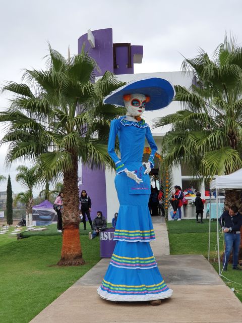 Figura gigante de una catrina con vestido azul y sombrero de ala ancha entre palmeras