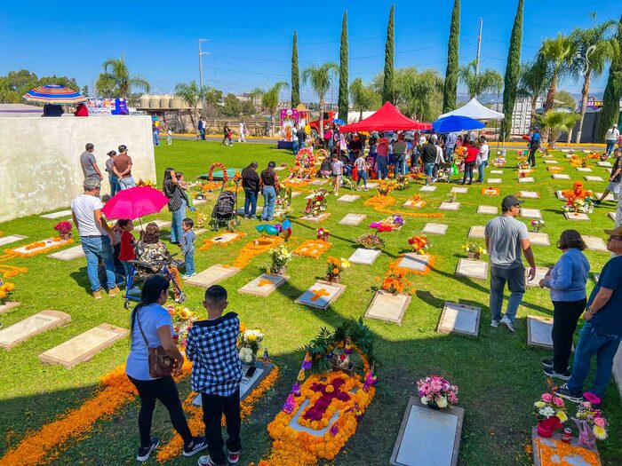 Visitantes entre placas conmemorativas adornadas con cempasúchil y arreglos florales