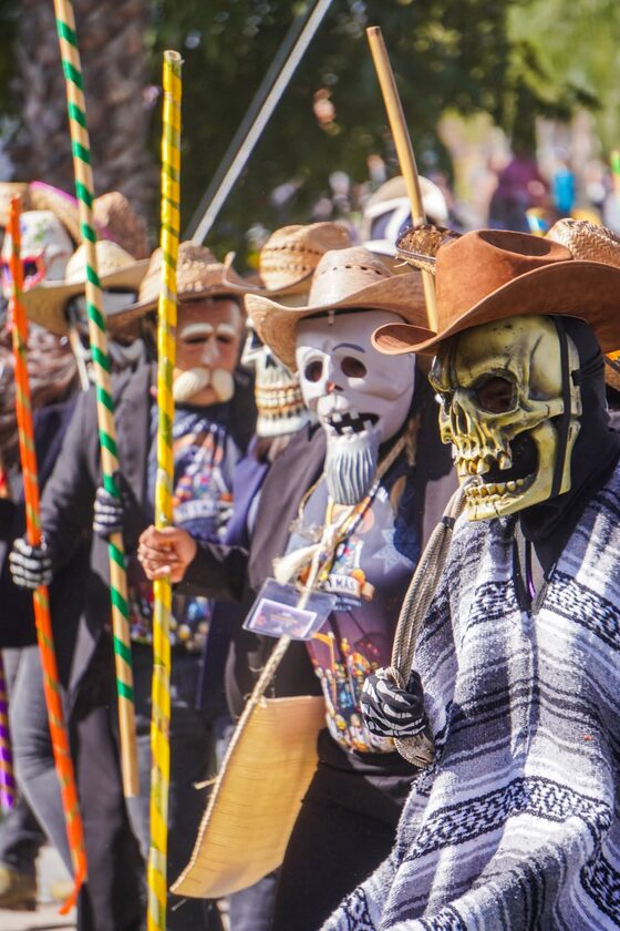 Integrantes de la comparsa de Xantolo con máscaras de calavera, sombreros y varas de colores