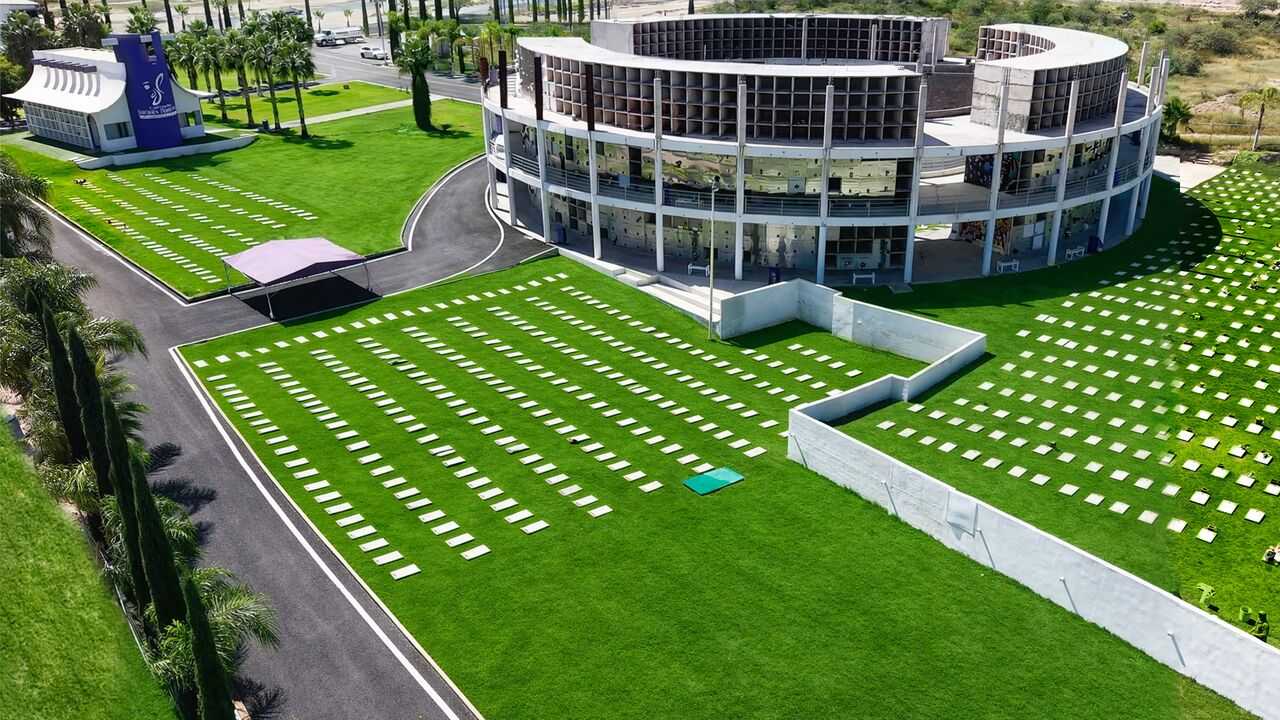 Vista aérea del cementerio Jardines Perpetuos: el edificio circular de mausoleos rodeado de jardines, placas en el césped y vialidades con palmeras y cipreses