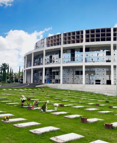 Fachada curva del edificio de nichos de Jardines Perpetuos vista desde el jardín, con las placas conmemorativas y sus floreros en el césped