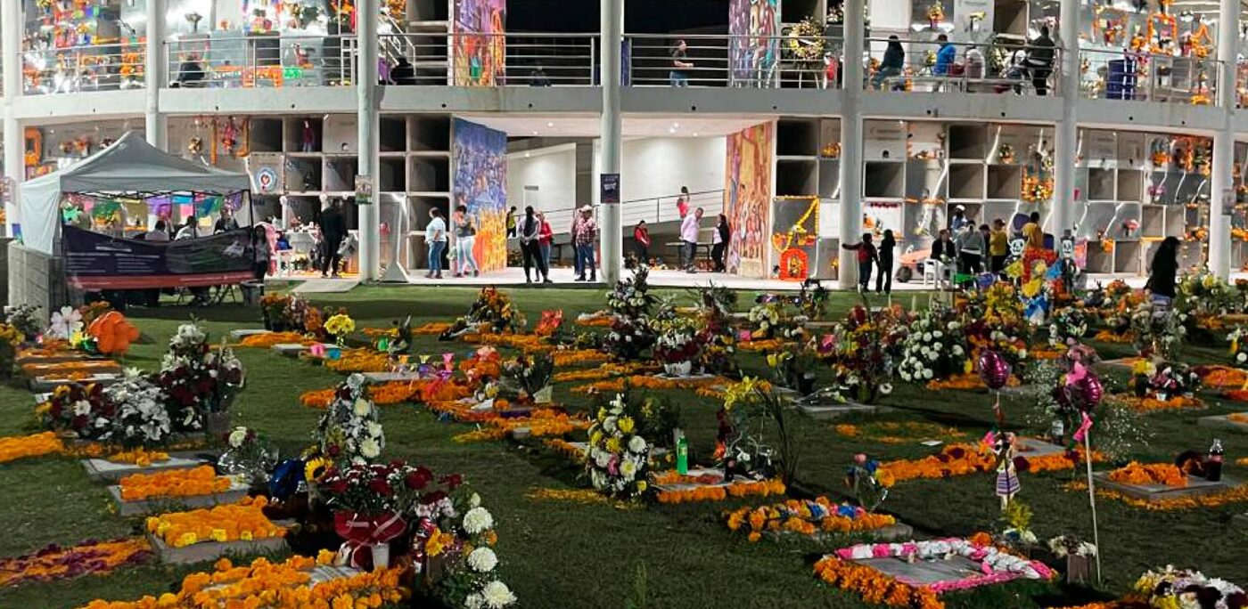 El edificio circular de nichos iluminado de noche durante el Día de Muertos, con las tumbas del jardín cubiertas de cempasúchil y flores